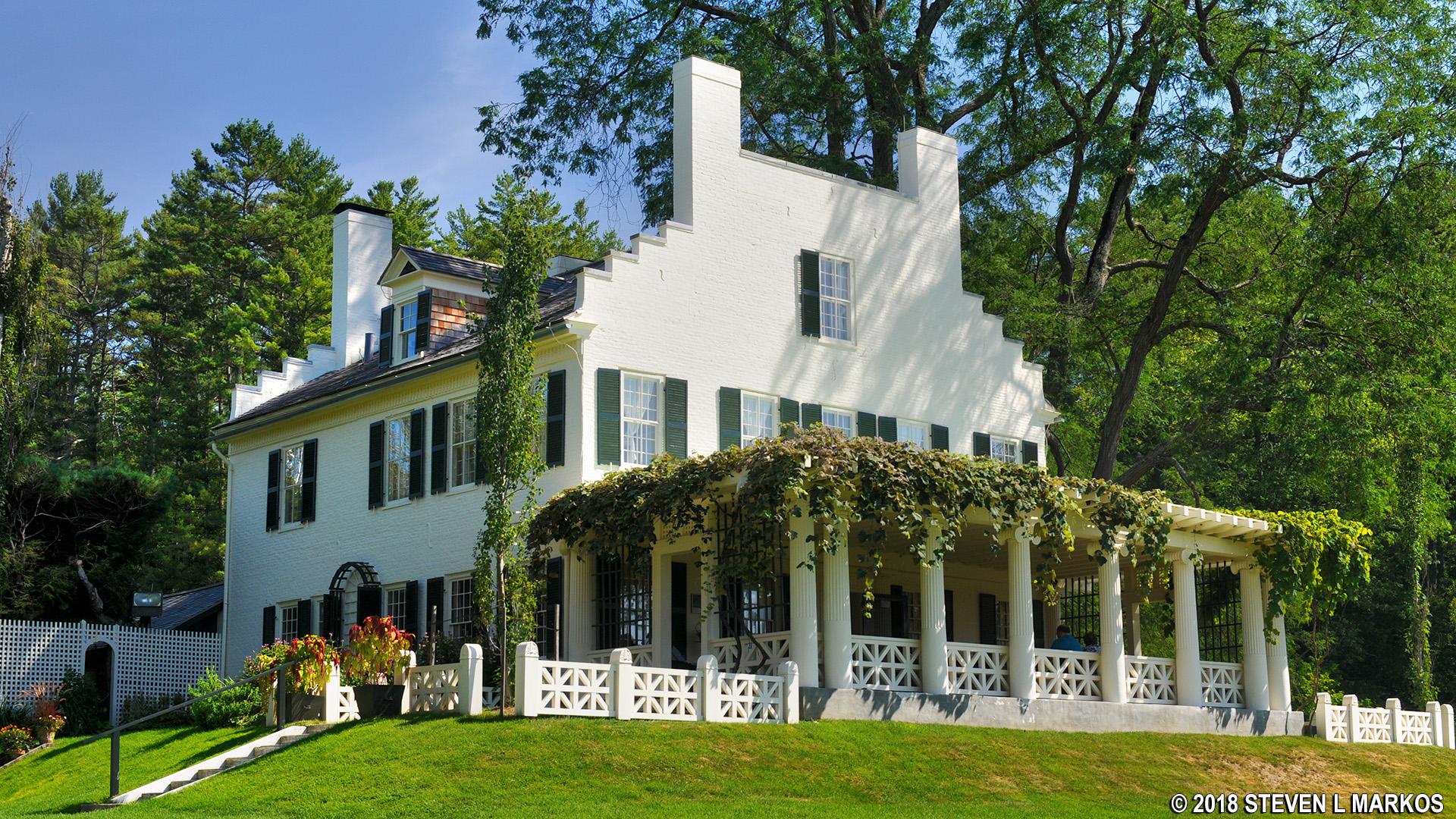 A large white house with a porch covered in vines in a green field