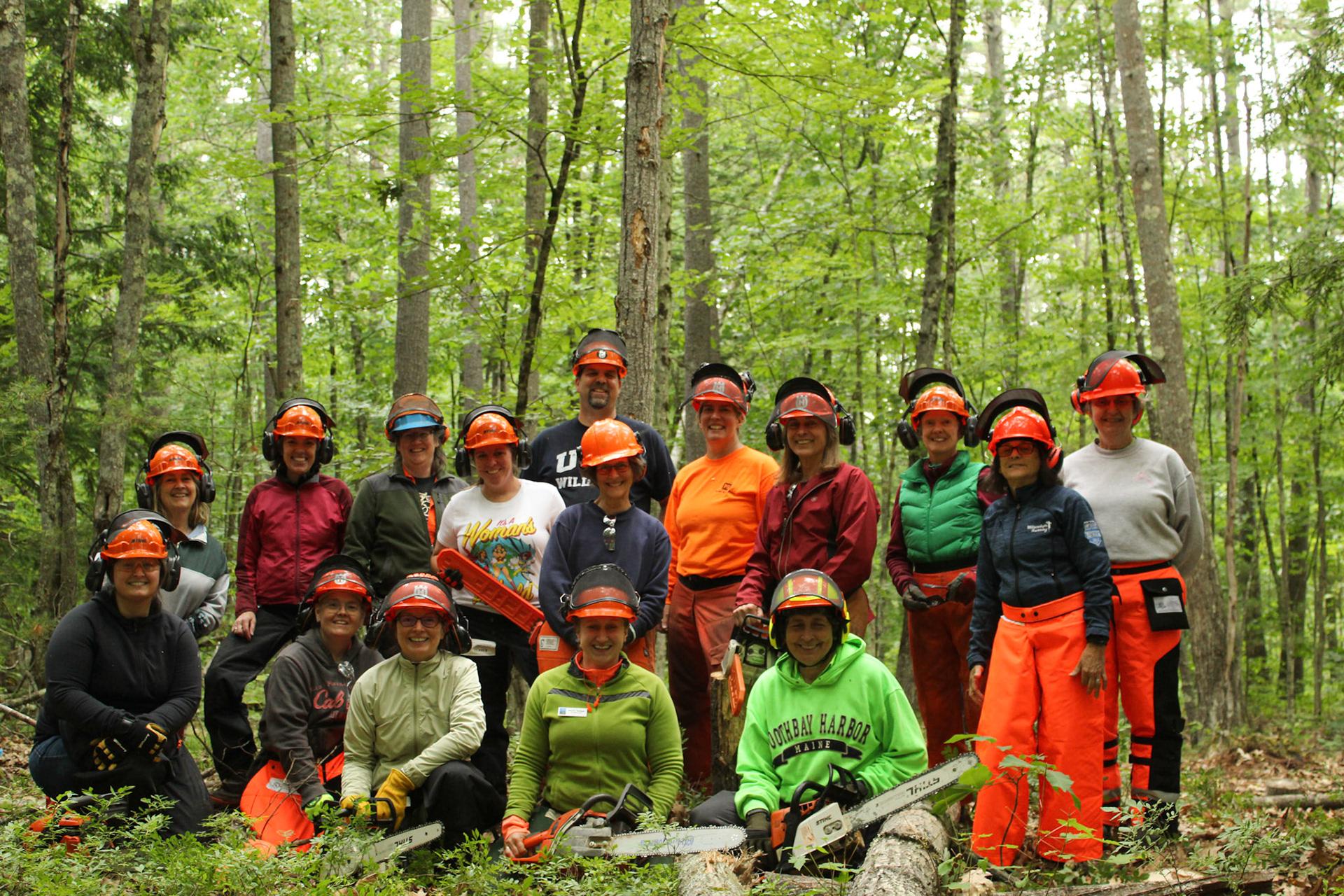 Group of people in personal protective equipment holding chainsaws seated in the forest