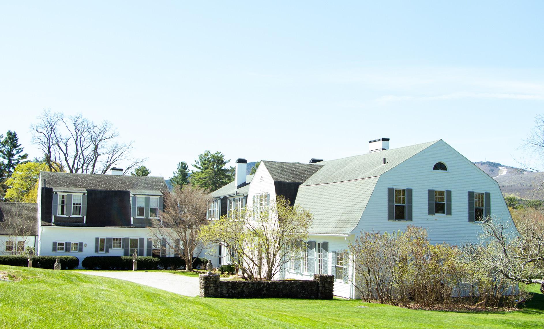 White house with green shutters on a green lawn in front of a small ski mountain