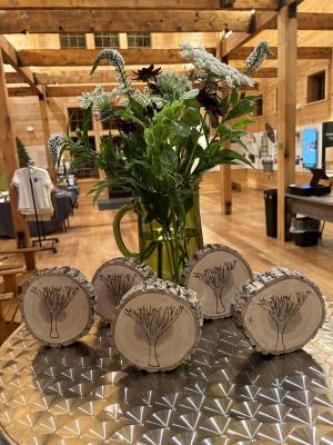 Five tree cookies with a tree etched into them on a table with a bouquet of flowers behind them. 