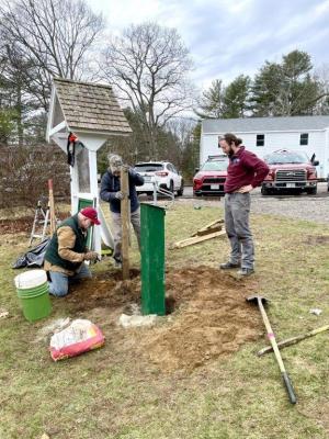 Three men work on installing a pair of sign posts. 