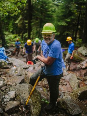 Trail volunteer poses with sledgehammer, eye protection, and a hardhat