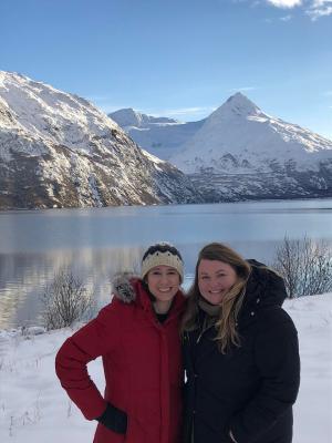 Two women in heavy coats stand in front of a snowy mountain