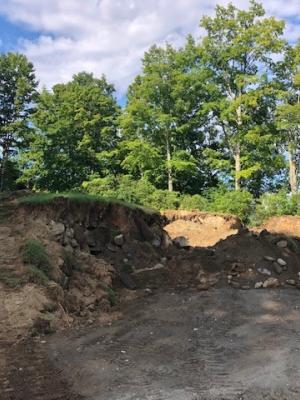 A dirt berm covered in grass and filled with soil and an old stone foundation is under construction.