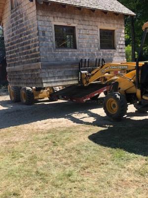 A small wood shed is lifted by a front-end loader.