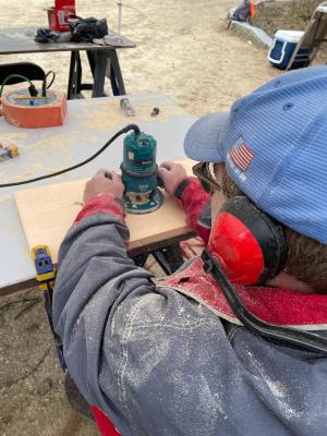 A man wearing red headphones maneuvers a router over a piece of wood. 