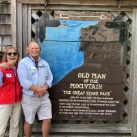 Jane in red and Dave in blue stand with historical sign for Old Man Mountains