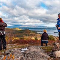 Hikers enjoying autumn view of Lake Winnipesaukee and Belknap Range from summit of Pine Mountain on Forest Society Morse Preserve