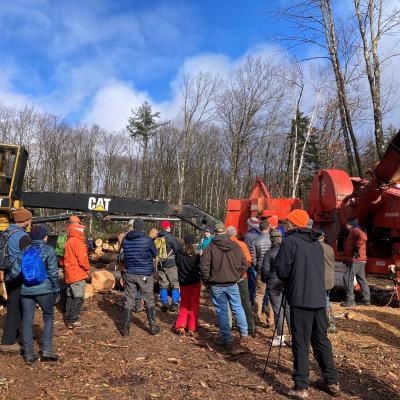 Photo showing the end of the tour with the group looking at a log pile, loader and chipper at the landing 