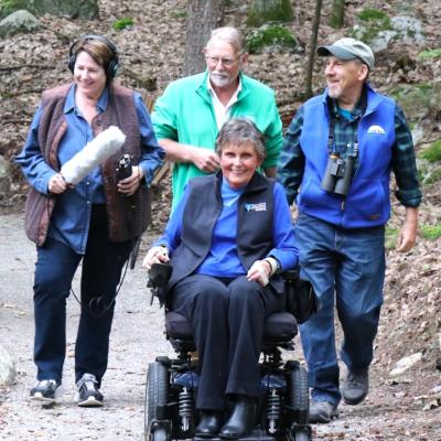 Three people and walking and one person is using a mobility scooter to traverse the trail.