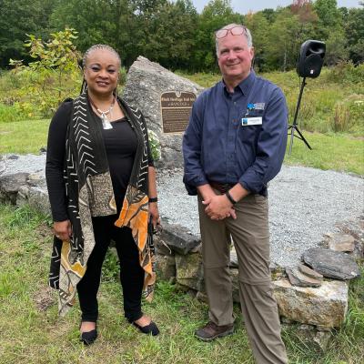 JerriAnne Boggis, Executive Director of the Black Heritage Trail of NH, and Jack Savage, President of the Forest Society, stand in front of the newly unveiled marker in Hancock under a blue sky.