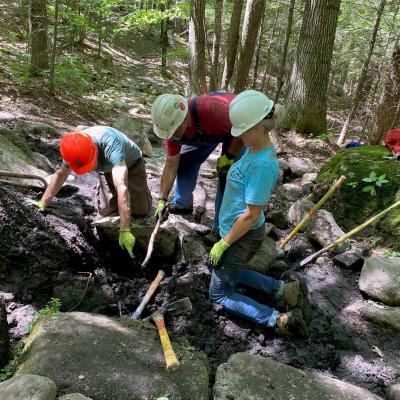 A group huddles around a muddy hole.