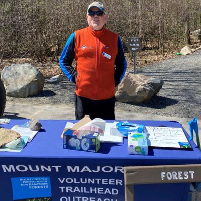 A volunteer stands at the VTOP table at the trailhead of Mt. Major.