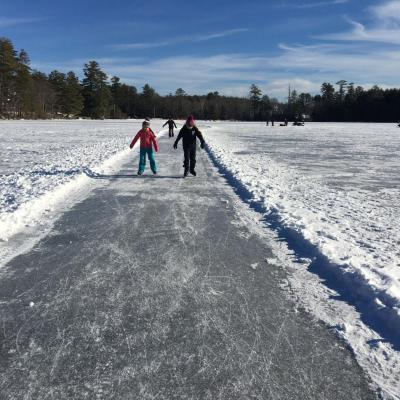 Children in winter clothes ice skate on a cleared path on a frozen lake 