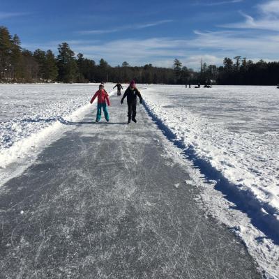 Children in winter clothes ice skate on a cleared path on a frozen lake 
