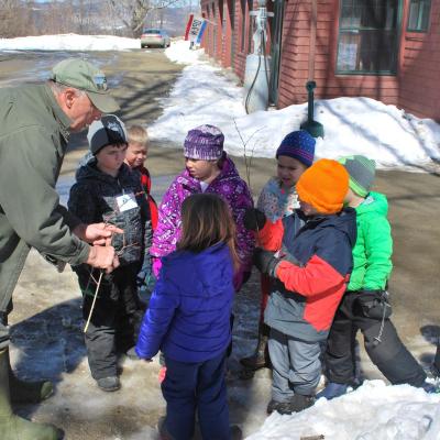 Young children gather around a guide during a maple tour.