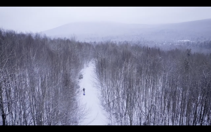 Aerial shot of winter forest with a xc skier moving down a trail 