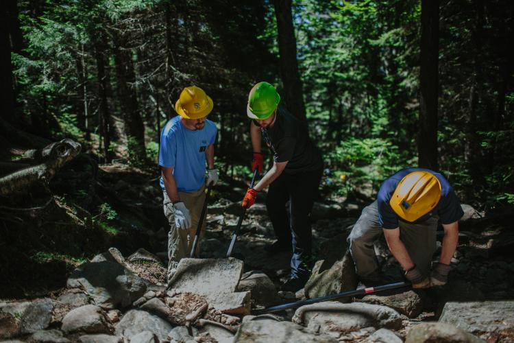 Volunteers use rock bars to place rocks that will help keep hikers on the trail