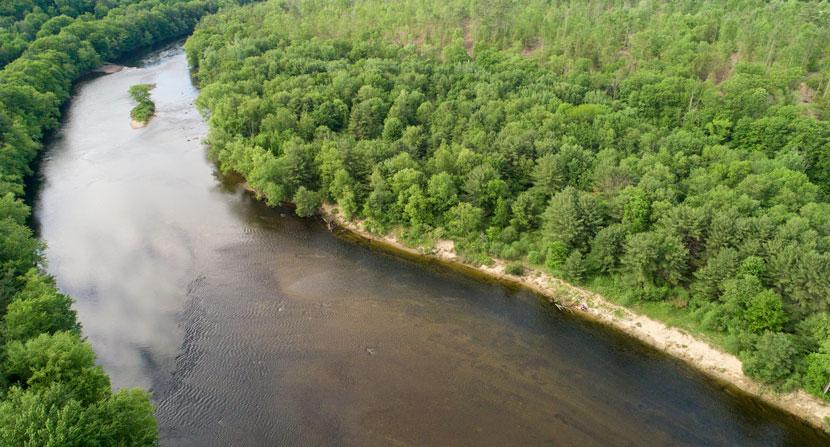 A bend in the Merrimack river lined with green trees from Stillhouse Forest.