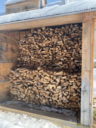 Cordwood piled neatly inside dry woodshed snow on roof
