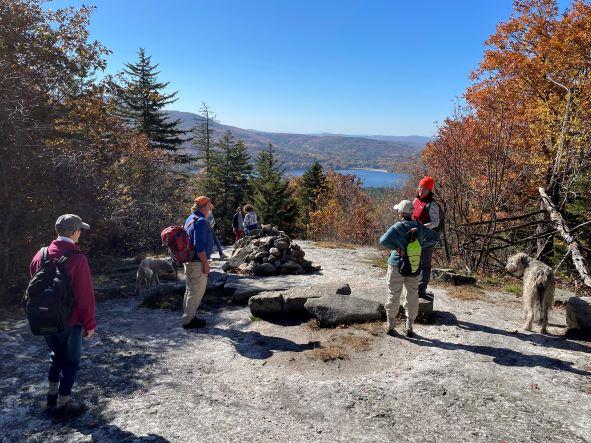 Open sky over granite summit with hikers and view of Lake Sunapee