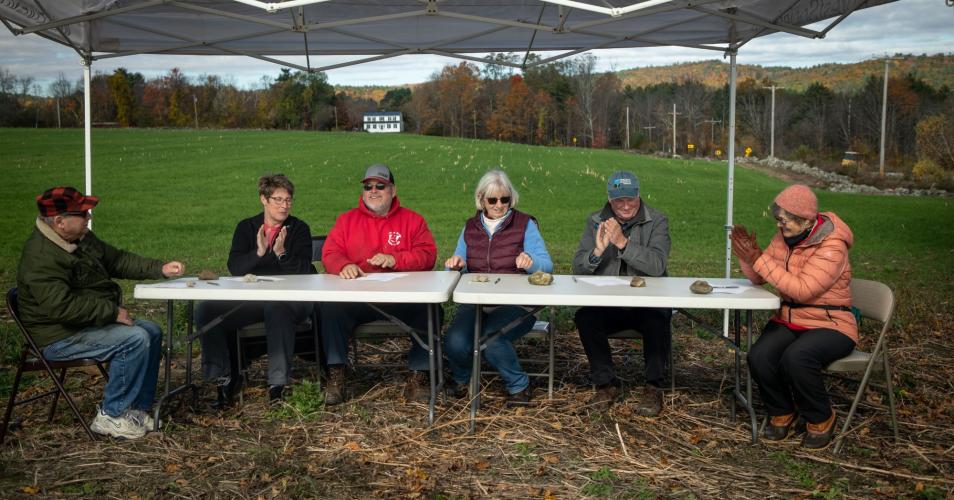 Members of the family sit at a table outdoors on the farm for the closing.
