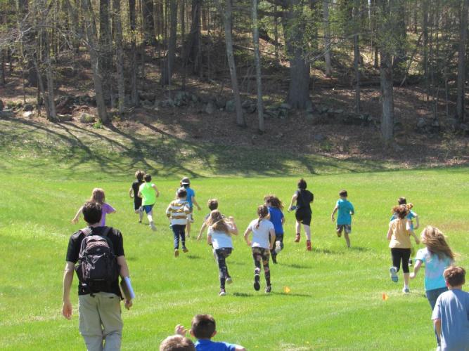 Student run across spring green field toward edge of pine woodland