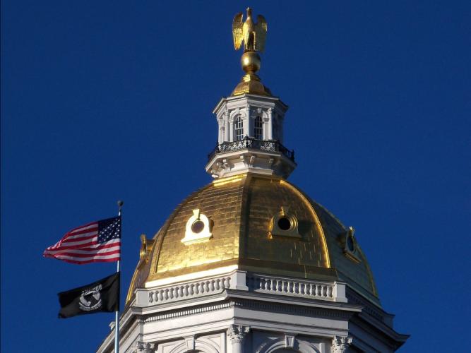 NH State Capital Dome against blue sky, American and POW flag waving